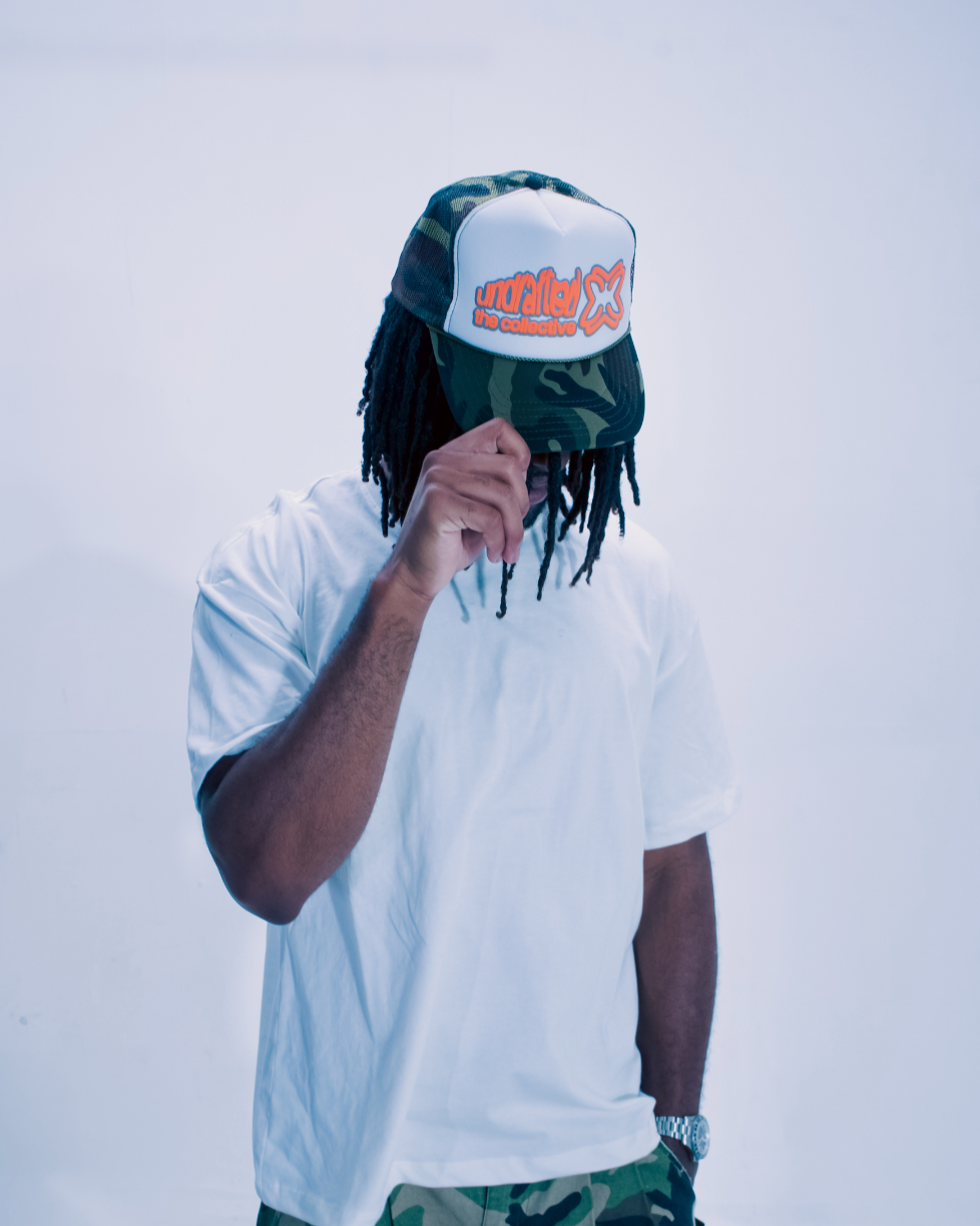 Person wearing a white t-shirt, camouflage pants, and a cap with a logo on a light gray background